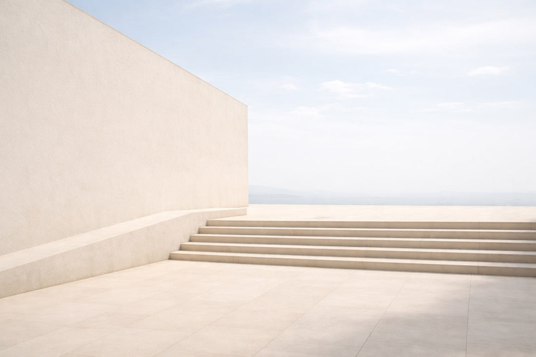 Helle, moderne Architekturfläche aus Beton und Putz im weichen Mittagslicht. Eine breite, flache Treppe führt über eine ruhige, offene Fläche ohne Menschen oder Objekte. Kaum Schatten, gleichmäßige Helligkeit,
