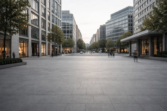 Moderner, weitläufiger Stadtplatz in einem gehobenen Viertel einer Großstadt am späten Nachmittag. Klare, funktionale Architektur, entsättigte Farben und gleichmäßiges, flaches Licht. Vereinzelte, entfernte Silhouetten