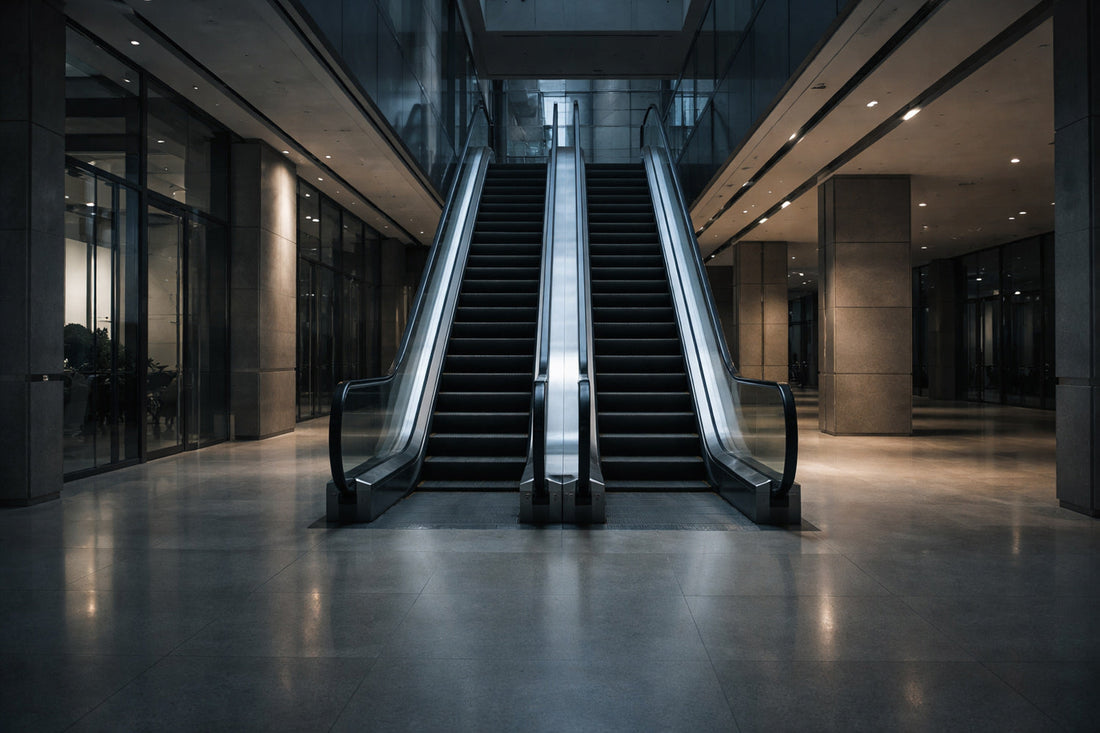 Leere, stehende Rolltreppe in einer modernen Büro- oder Mallarchitektur am späten Nachmittag. Klare Linien aus Glas, Stein und Metall, kühles, sachliches Licht. Keine Menschen, keine Bewegung.