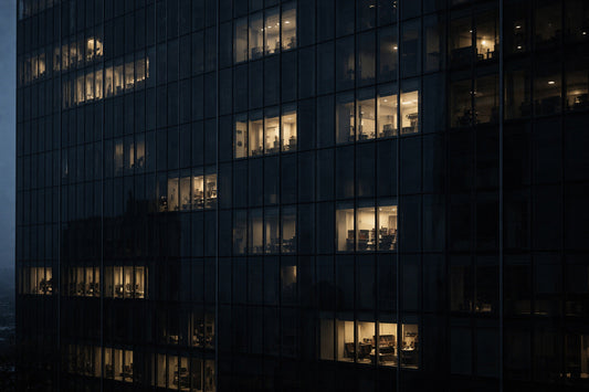 Moderne Hochhausfassade in der Dämmerung, dunkles Glas mit vereinzelten erleuchteten Bürofenstern. Die Architektur wirkt funktionierend und aktiv, obwohl kein Mensch sichtbar ist – Arbeit scheint weiterzulaufen.