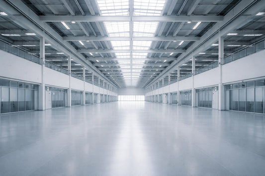 Große, moderne Halle mit serieller Architektur und gleichmäßigem Tageslicht von oben. Die symmetrische Struktur aus Stahl, Glas und Beton wirkt offen, richtungslos und leer – ein Raum ohne Markierung.