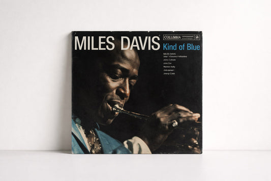 Frontal aufgenommenes Plattencover „Kind of Blue“ von Miles Davis vor neutralem, hellem Hintergrund. Gleichmäßiges Vormittagslicht, sichtbare Papierstruktur und leichte Gebrauchsspuren.