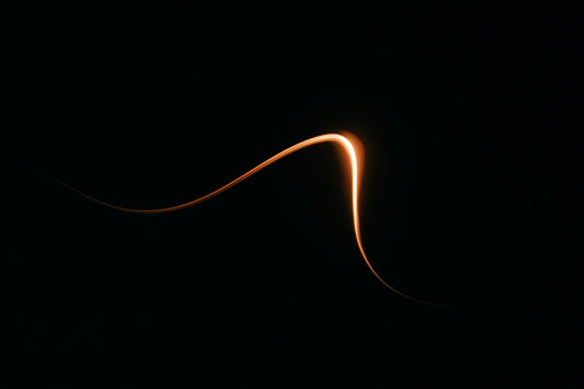 Eine geschwungene, glühende Lichtspur vor dunklem Hintergrund – wie eine sichtbar gewordene Bewegung durch die Zeit.