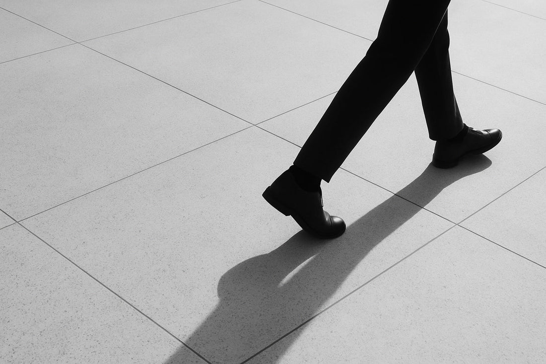 Diagonal verlaufender Schatten eines gehenden Menschen auf hellem Steinboden; nur Beine und Bewegung sichtbar, reduziertes Schwarz-Weiß, ruhig und offen ohne Ziel.