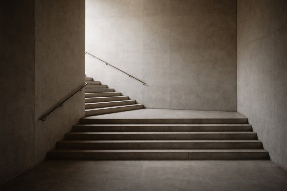 Schlichte, breite Treppe aus hellem Stein in einem urbanen Innenraum. Die Stufen führen ohne erkennbare Richtung nach oben, seitlich begrenzt von glatten Wänden. Ruhiges, flaches Spätnachmittagslicht