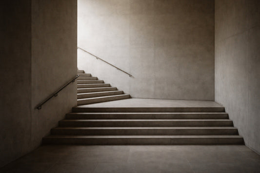 Schlichte, breite Treppe aus hellem Stein in einem urbanen Innenraum. Die Stufen führen ohne erkennbare Richtung nach oben, seitlich begrenzt von glatten Wänden. Ruhiges, flaches Spätnachmittagslicht