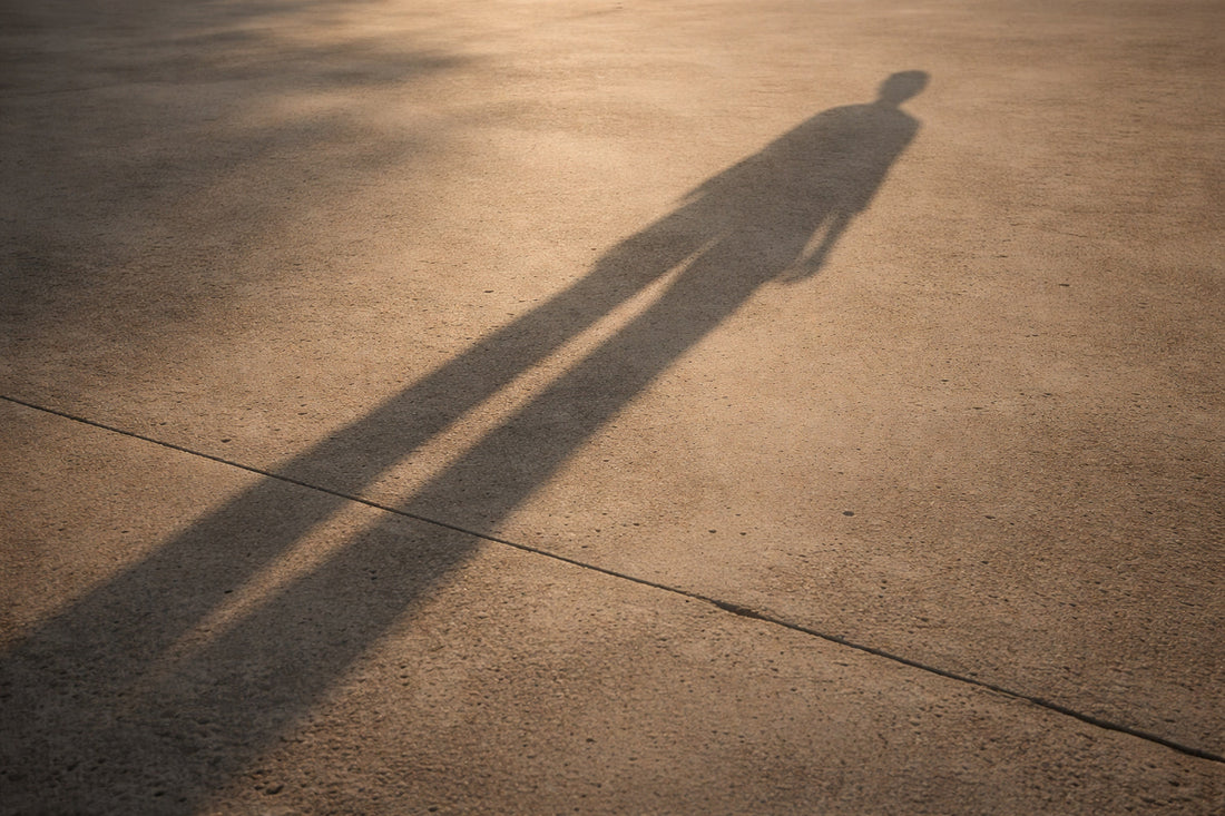 Langer, scharf gezeichneter Menschenschatten auf heller Betonfläche im warmen Abendlicht, hohe Perspektive, ruhige Fläche ohne sichtbare Person.