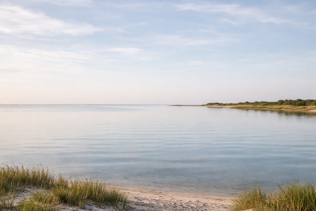 Ruhige Küstenlandschaft mit flachem Horizont, stillem Wasser und hellem Himmel. Das Wasser liegt fast unbewegt, die Küstenlinie zieht sich leise in die Ferne. Keine Menschen, keine Boote,