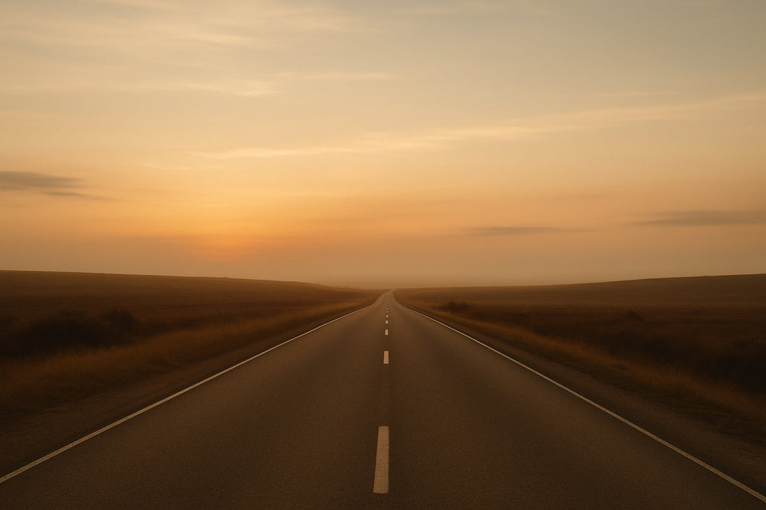 Lange, gerade Landstraße im warmen Abendlicht, die in einen goldenen Horizont führt. Weiche Schatten liegen über den Feldern, der Himmel zeigt sanfte Gold- und Orangetöne. Ruhige, weite Szene eines stillen Heimwegs.