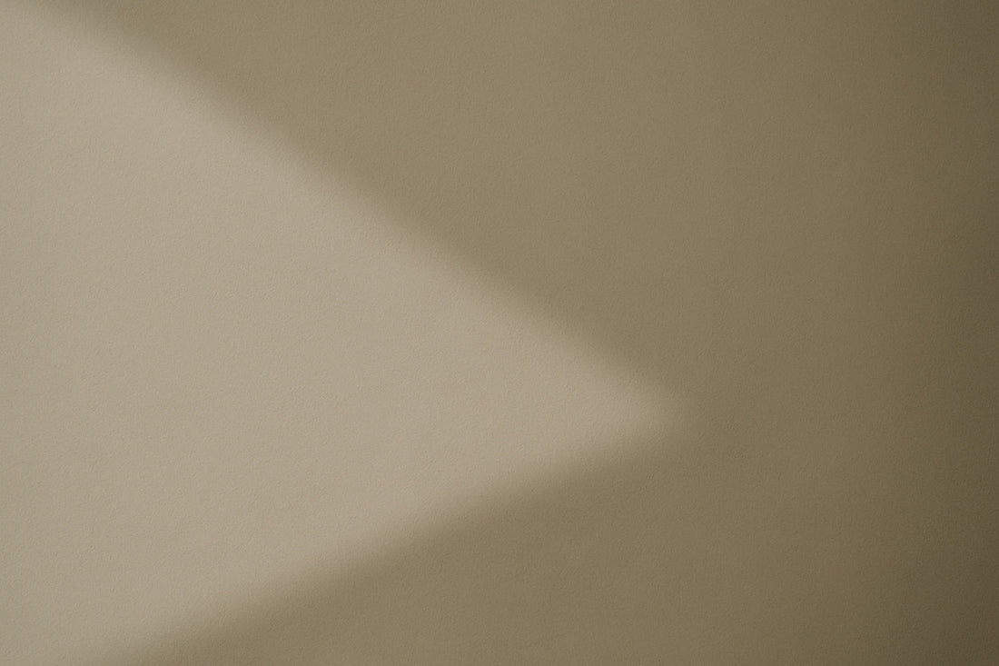 Weicher diagonaler Schatten auf warmgrauer, leicht strukturierter Wandfläche; abstrakte, ruhige Lichtkomposition im minimalistischen Ombra-Celeste-Editorialstil.