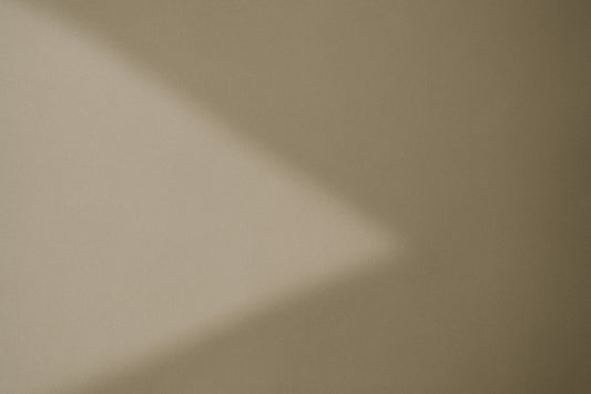 Weicher diagonaler Schatten auf warmgrauer, leicht strukturierter Wandfläche; abstrakte, ruhige Lichtkomposition im minimalistischen Ombra-Celeste-Editorialstil.