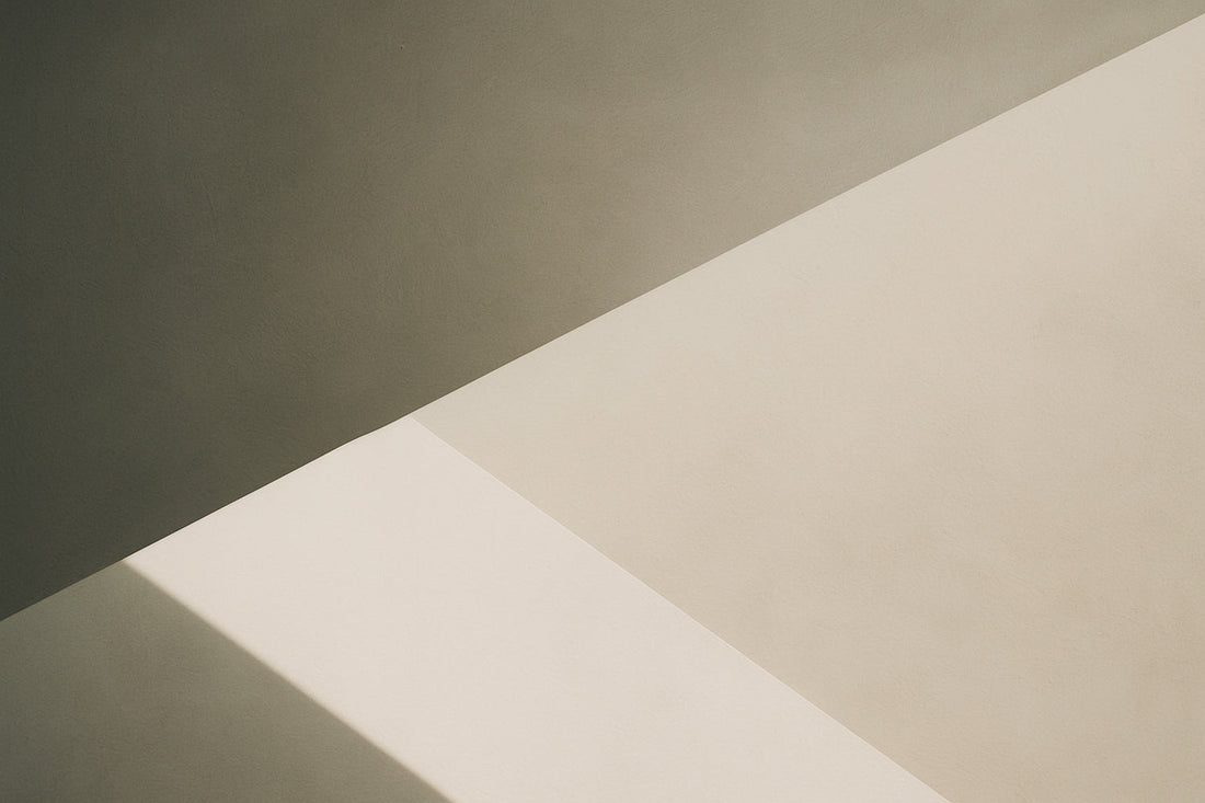 Abstrakte geometrische Komposition mit klarer, diagonaler Lichtkante; oben eine dunklere warmgraue Fläche, unten helle beige Fläche mit präziser Schattenlinie