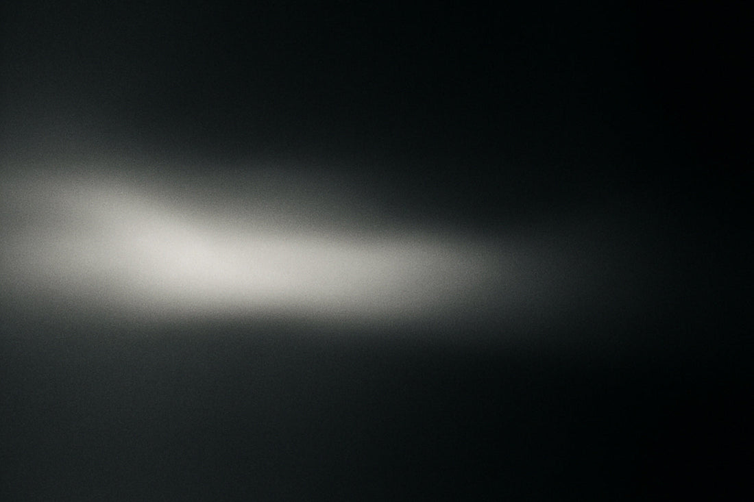 tiefdunkler Raum aus, mit sanften Übergängen von hellem Weiß zu gedämpftem Grau; filmische Körnung und subtile Unschärfe erzeugen eine ruhige, atmosphärische Szene im hochgradig reduzierten Ombra-Celeste-Editorial-Stil.