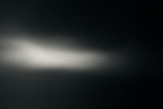 tiefdunkler Raum aus, mit sanften Übergängen von hellem Weiß zu gedämpftem Grau; filmische Körnung und subtile Unschärfe erzeugen eine ruhige, atmosphärische Szene im hochgradig reduzierten Ombra-Celeste-Editorial-Stil.