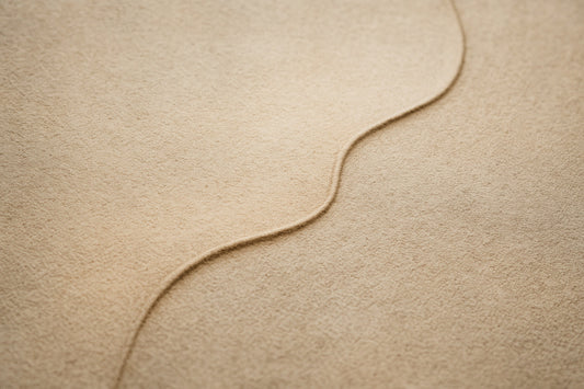 Organische, feine Linie auf warmer, sandfarbener Struktur. Die weiche Kurve wirkt wie eine Spur im Material – ruhig, poetisch, minimalistisch, mit Gefühl von Richtung und Leichtigkeit