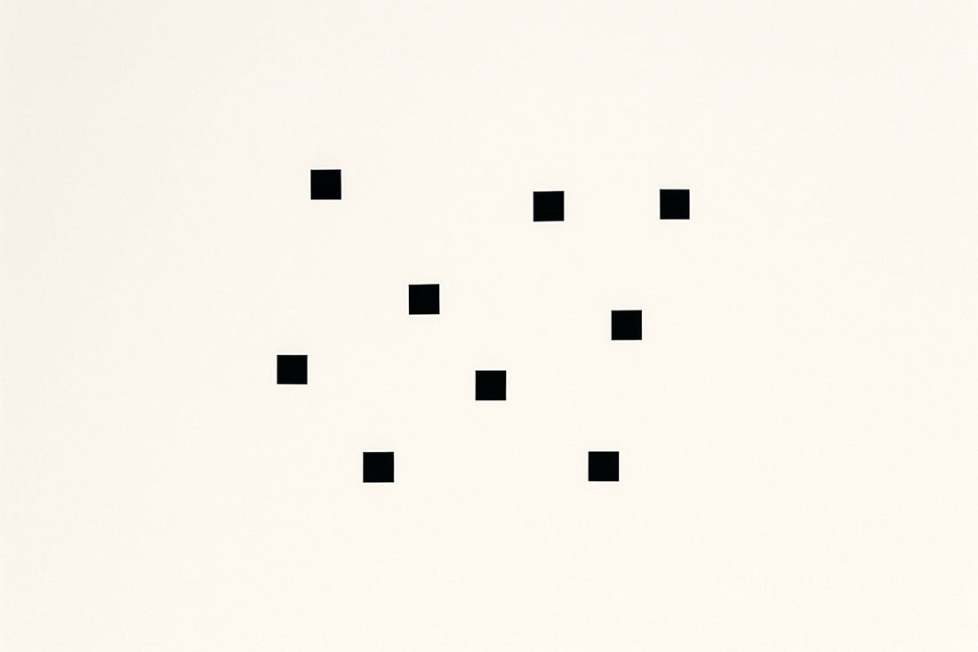 Helles, fast cremefarbenes Feld mit neun kleinen schwarzen Quadraten, unregelmäßig verteilt wie digitale Fragmente oder Pixel in Auflösung. Minimalistische, moderne Medienkunst-Ästhetik mit klaren Formen und ruhiger, reduzierter Komposition