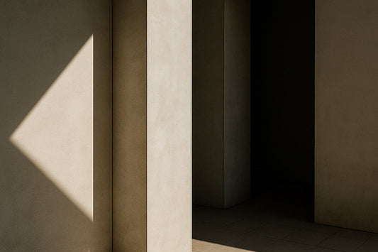 Ein stiller, minimalistischer Innenraum mit weichen beige-grauen Wänden: diagonales Sonnenlicht wirft ein scharfes, dreieckiges Lichtfragment auf eine Wand, während ein hoher Pfeiler und ein dunkler Durchgang tiefe Schatten erzeugen.